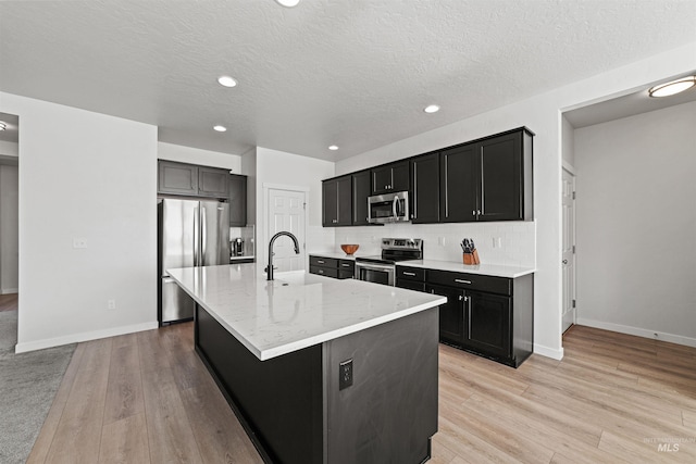 kitchen with tasteful backsplash, an island with sink, sink, light hardwood / wood-style floors, and stainless steel appliances