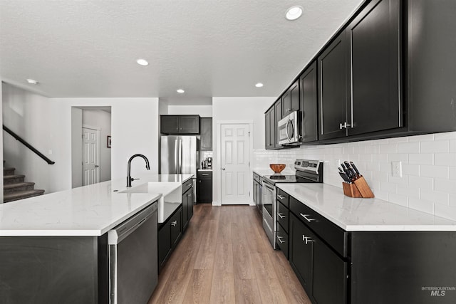 kitchen with sink, tasteful backsplash, appliances with stainless steel finishes, an island with sink, and hardwood / wood-style floors