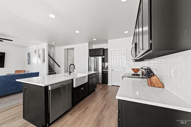 kitchen featuring an island with sink, appliances with stainless steel finishes, sink, and light wood-type flooring