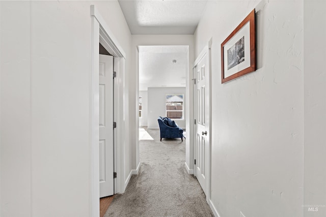 corridor with light carpet and a textured ceiling