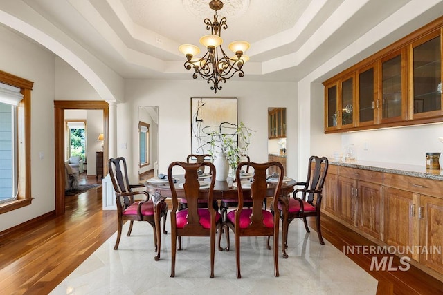 4553 N Arrow Crest Way, Boise, ID 83703 - dining room with a tray ceiling, arched walkways, a chandelier, and light wood-type flooring
