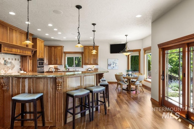 4553 N Arrow Crest Way, Boise, ID 83703 - kitchen featuring a textured ceiling, backsplash, brown cabinetry, a breakfast bar area, and recessed lighting