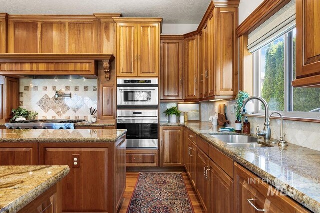 4553 N Arrow Crest Way, Boise, ID 83703 - kitchen featuring a sink, brown cabinets, appliances with stainless steel finishes, dark wood-style flooring, and backsplash