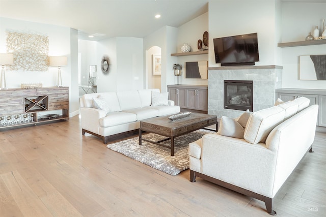 living room with a tile fireplace, arched walkways, recessed lighting, and wood finished floors