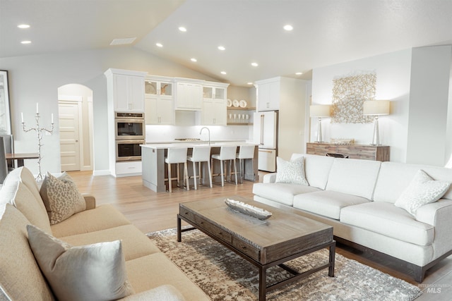 living room with light wood finished floors, recessed lighting, visible vents, arched walkways, and lofted ceiling