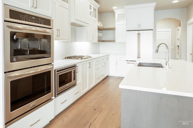 kitchen with a sink, built in appliances, backsplash, light countertops, and arched walkways