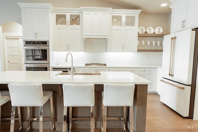 kitchen with tasteful backsplash, open shelves, appliances with stainless steel finishes, a breakfast bar, and light countertops