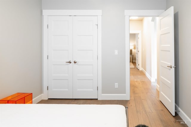 bedroom with a closet, light wood-style flooring, and baseboards