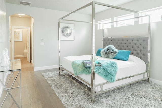 bedroom with arched walkways, visible vents, wood finished floors, and baseboards