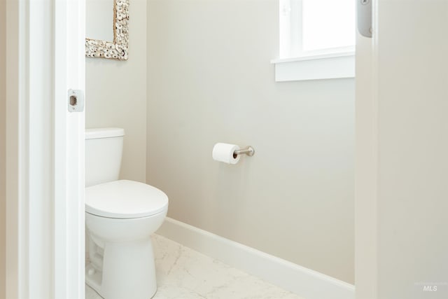bathroom with toilet, marble finish floor, and baseboards