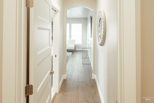 hallway with light wood finished floors, arched walkways, and baseboards