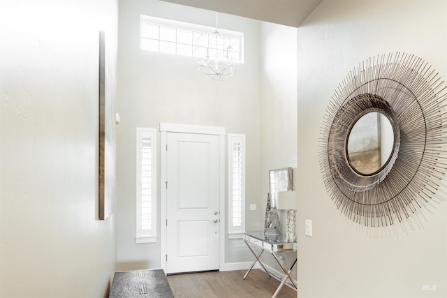 foyer featuring a wealth of natural light, wood finished floors, a towering ceiling, and a notable chandelier