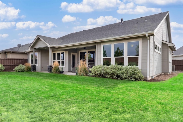 back of property featuring fence, roof with shingles, and a lawn