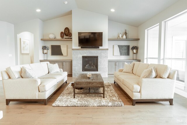 living room with arched walkways, a tile fireplace, recessed lighting, vaulted ceiling, and wood finished floors