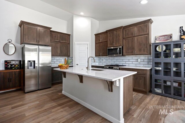 kitchen with sink, a kitchen island with sink, dark hardwood / wood-style floors, tasteful backsplash, and stainless steel appliances