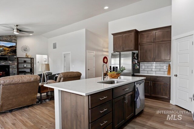 kitchen featuring light hardwood / wood-style flooring, stainless steel appliances, tasteful backsplash, ceiling fan, and a stone fireplace