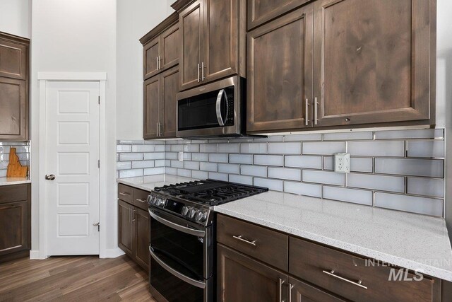 kitchen with decorative backsplash, dark hardwood / wood-style flooring, appliances with stainless steel finishes, light stone counters, and dark brown cabinets