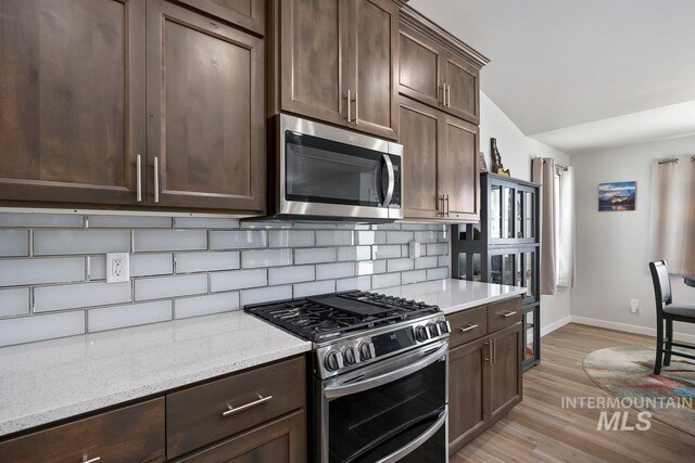 kitchen with light wood-type flooring, a stone fireplace, dishwasher, sink, and lofted ceiling