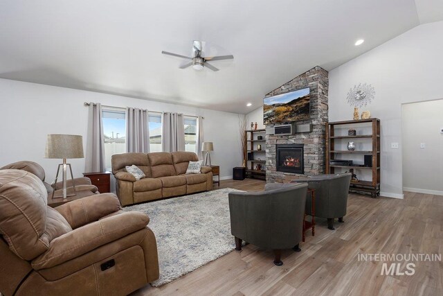 living room with light hardwood / wood-style floors, vaulted ceiling, and a stone fireplace