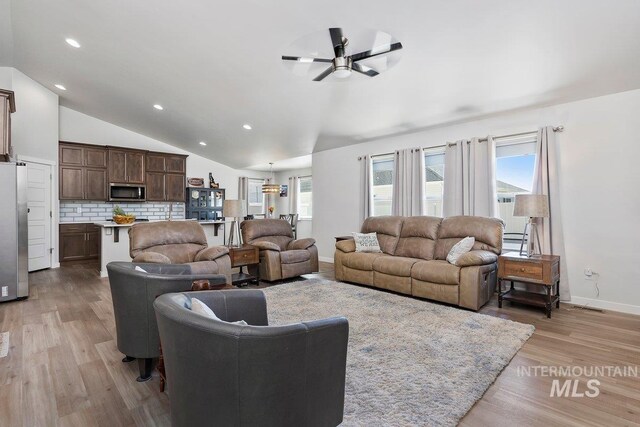 living room with ceiling fan, vaulted ceiling, and light hardwood / wood-style flooring