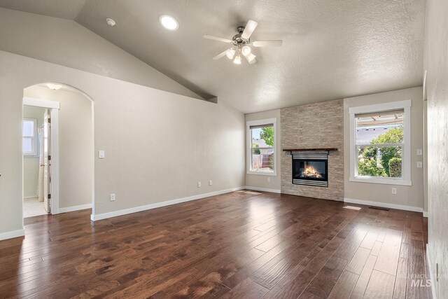 613 E Sable Ridge Dr, Kuna, ID 83634 - unfurnished living room with a ceiling fan, arched walkways, lofted ceiling, dark wood finished floors, and a stone fireplace