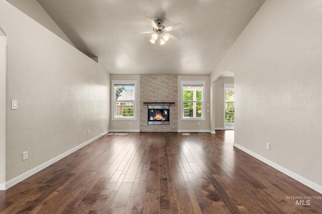 613 E Sable Ridge Dr, Kuna, ID 83634 - unfurnished living room with arched walkways, lofted ceiling, dark wood-type flooring, ceiling fan, and a stone fireplace
