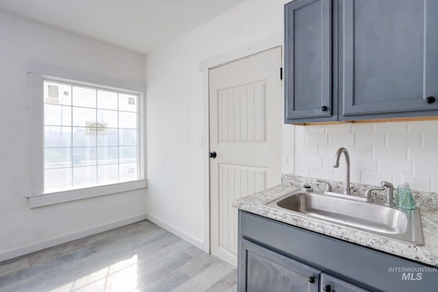 kitchen with tasteful backsplash, baseboards, light wood-style flooring, light countertops, and a sink