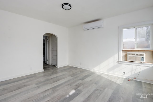 unfurnished room with arched walkways, cooling unit, an AC wall unit, and wood finished floors