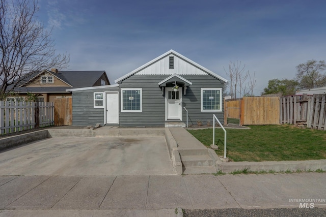 bungalow with board and batten siding, fence, and a front lawn