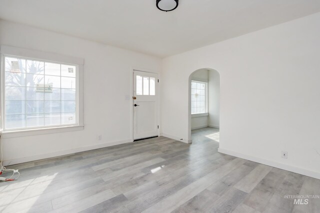 interior space featuring arched walkways, baseboards, and light wood-style floors