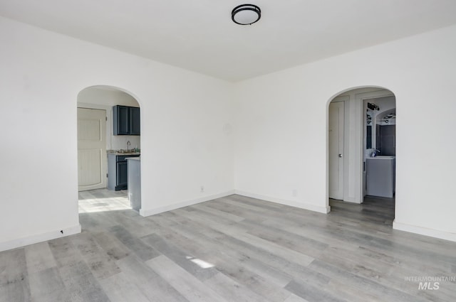 spare room with arched walkways, baseboards, and light wood-type flooring