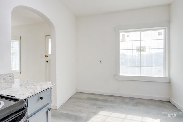 unfurnished dining area with arched walkways, light wood-type flooring, and baseboards