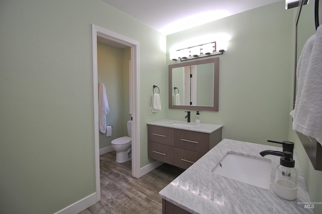 full bath with a sink, toilet, two vanities, and wood finished floors