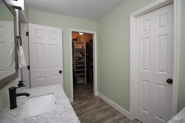 bathroom featuring baseboards, vanity, wood finished floors, and a spacious closet