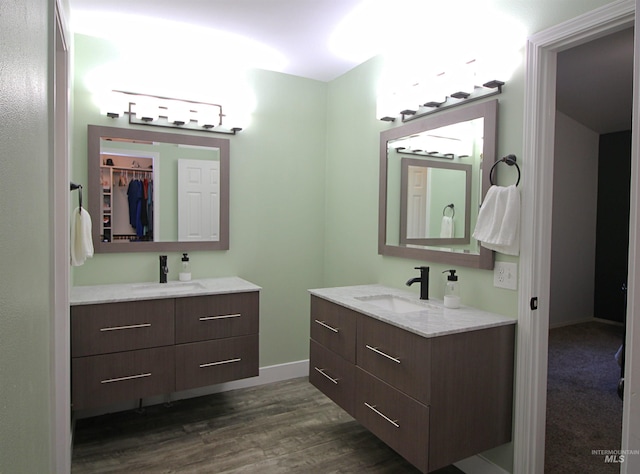 full bath featuring a sink, baseboards, two vanities, and wood finished floors