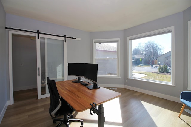 home office with baseboards, dark wood-type flooring, and a barn door