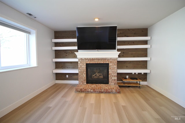 unfurnished living room featuring wood finished floors, a fireplace, visible vents, and baseboards