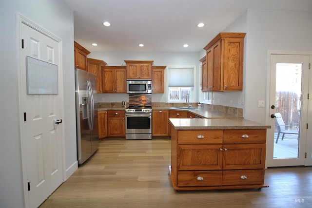 kitchen with a peninsula, brown cabinets, appliances with stainless steel finishes, and a sink