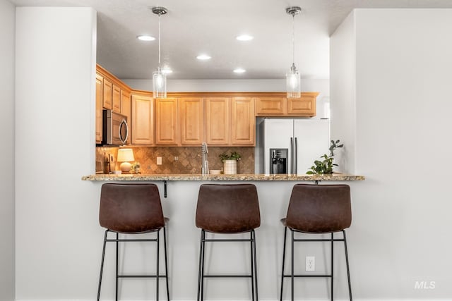 kitchen featuring decorative backsplash, stainless steel microwave, light stone counters, a breakfast bar area, and fridge with ice dispenser