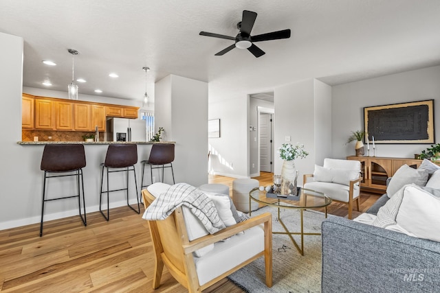 living area with a ceiling fan, recessed lighting, baseboards, and light wood-type flooring
