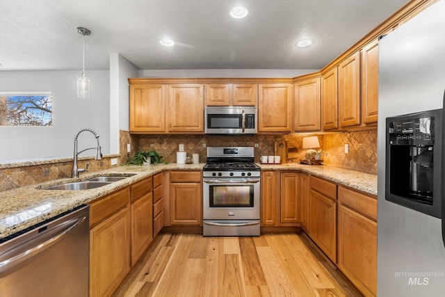 kitchen with light stone countertops, tasteful backsplash, appliances with stainless steel finishes, a sink, and light wood-type flooring
