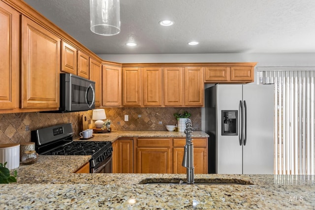 kitchen featuring a sink, stainless steel appliances, tasteful backsplash, and light stone counters