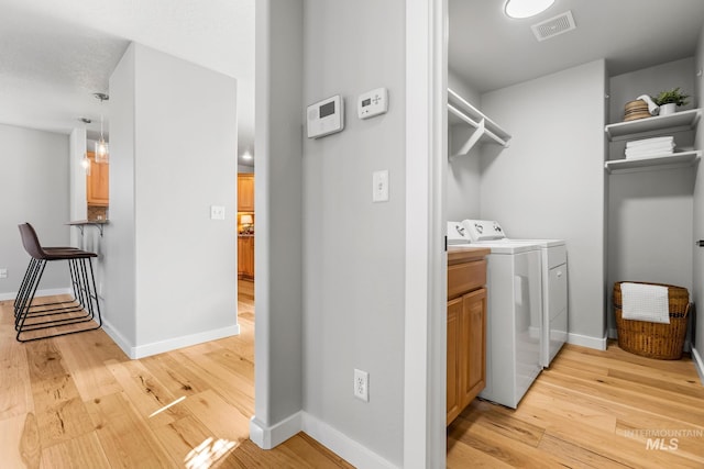 washroom featuring washing machine and clothes dryer, light wood-style flooring, baseboards, visible vents, and cabinet space