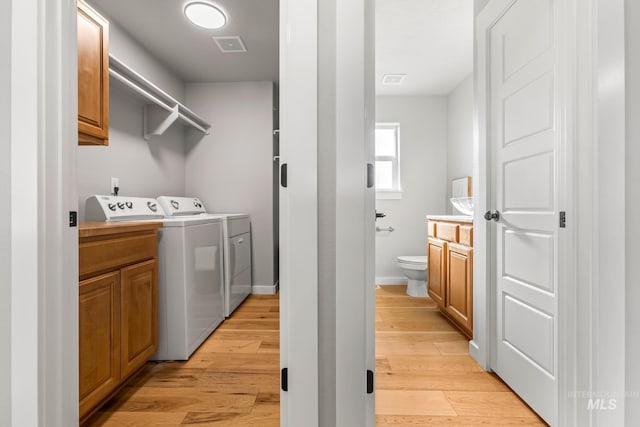 laundry area with light wood finished floors, washer and clothes dryer, visible vents, and cabinet space