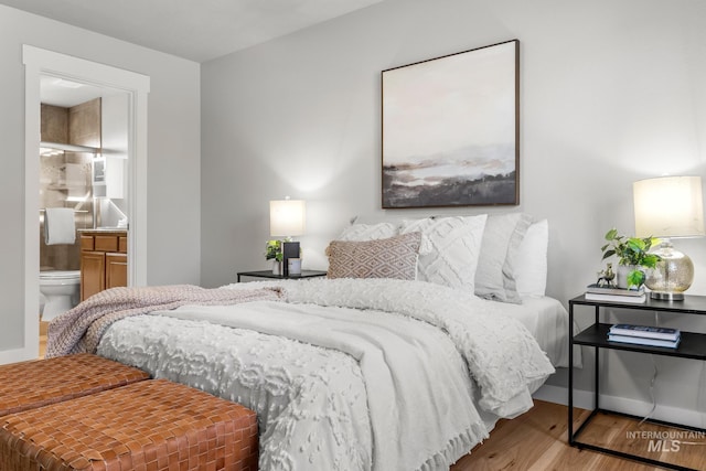 bedroom featuring baseboards, ensuite bathroom, and wood finished floors