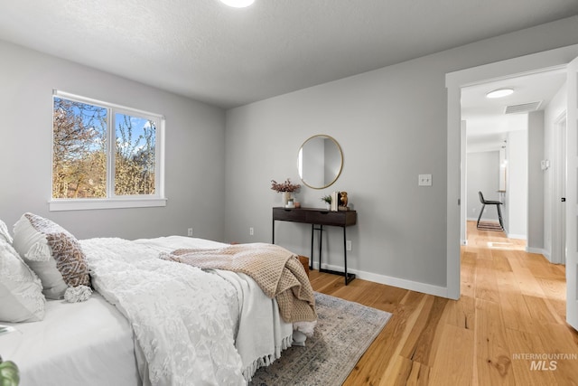 bedroom with baseboards, light wood-style floors, a textured ceiling, and visible vents