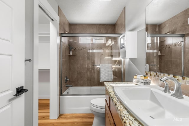 full bathroom with toilet, vanity, shower / bath combination with glass door, and wood finished floors