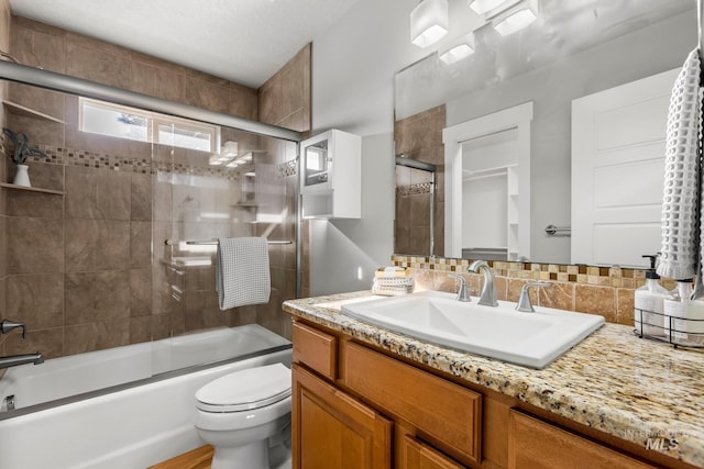 bathroom featuring backsplash, toilet, vanity, and bath / shower combo with glass door