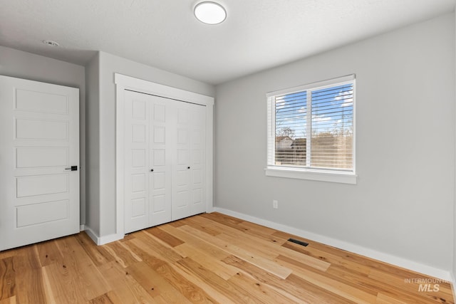 unfurnished bedroom with light wood finished floors, baseboards, visible vents, and a closet