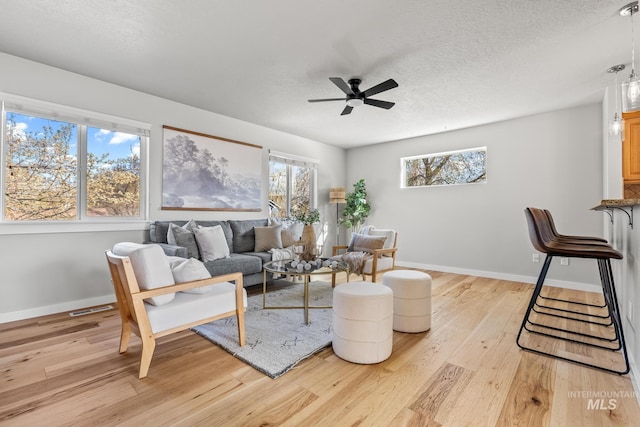 living area featuring a ceiling fan, a healthy amount of sunlight, light wood-style flooring, and a textured ceiling